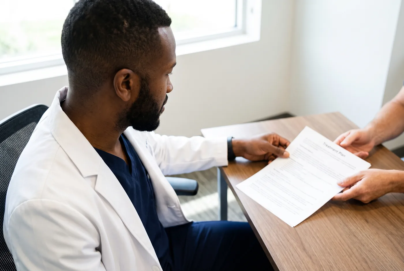 Dr. Peter K. Cudjoe passing a printed treatment plan across a desk to a patient